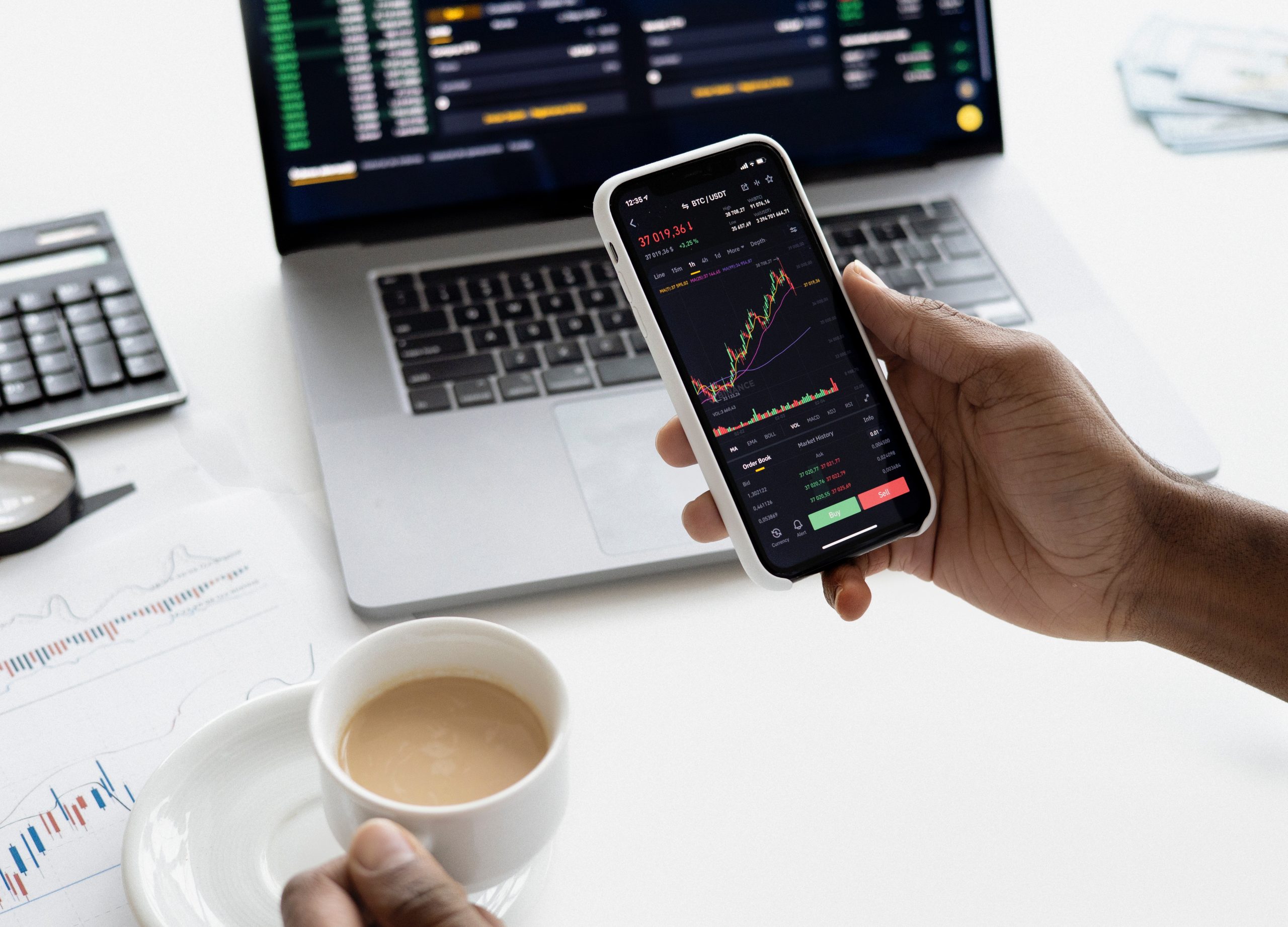 person looking at stock charts while holding a cup of coffee