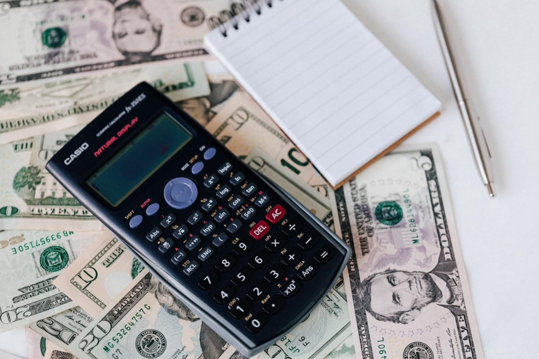 a calculator and note pad on top of a pile of money